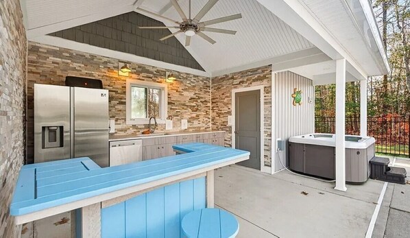 A covered outdoor kitchen area with a built-in refrigerator, a bar counter, and a hot tub.