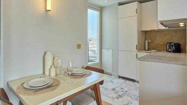 A modern kitchen with white cabinets, a coffee machine, and a dining area with a table set for two. - Charming Apartment in Beaubourg - Le Marais (Paris)