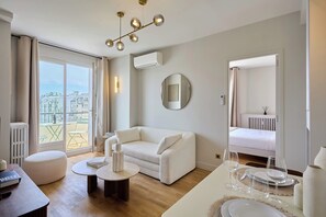 A modern living room with a white sofa, a round mirror, and a dining table set with glasses and plates. - Charming Apartment in Beaubourg - Le Marais (Paris)