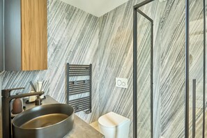 A modern bathroom with a marble-patterned wall, a black sink, a white toilet, and a black towel rack. - Charming Apartment in Beaubourg - Le Marais (Paris)