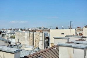 A cityscape with multiple rooftops, some with visible chimneys and antennas, and a clear sky. - Charming Apartment in Beaubourg - Le Marais (Paris)
