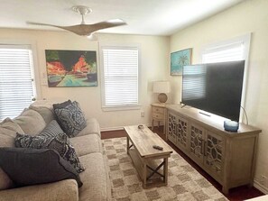 Ein Wohnzimmer mit einer Couch, einem Couchtisch, einem Fernseher und Kunstwerken an den Wänden.