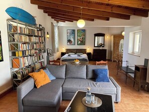 Ein Wohnzimmer mit Sofa, Couchtisch, Bücherregal, einem Bett und einem Essbereich.