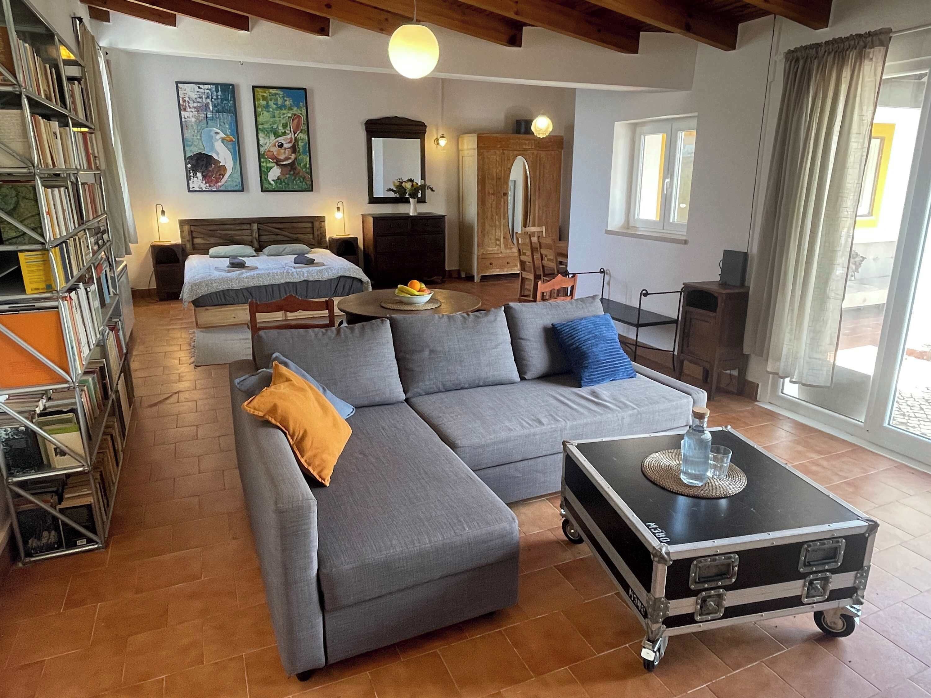 Una sala de estar con sofá, mesa de centro, estantería, cama y comedor.