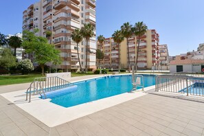 Une piscine dotée d’une terrasse carrelée, entourée de palmiers et d’immeubles d’habitation.