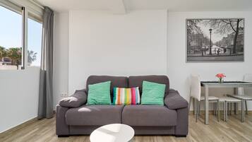 A modern living room with a grey sofa, a small white table, and a dining area with chairs and a table.