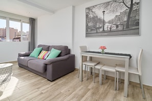 Uma sala de estar moderna com um sofá cinzento, uma mesa de jantar com cadeiras, uma janela com cortinas e uma pintura com paisagem urbana na parede.