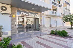 Un bâtiment avec une entrée en verre, une enseigne indiquant « PLAZAMAR », et un parking en arrière-plan.