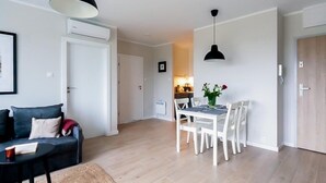 A modern living room with a sofa, a dining table with chairs, a hanging light fixture, and a door leading to another room. - Spacious Comfy Apartment for 5 Dziwnow (Dziwnów)