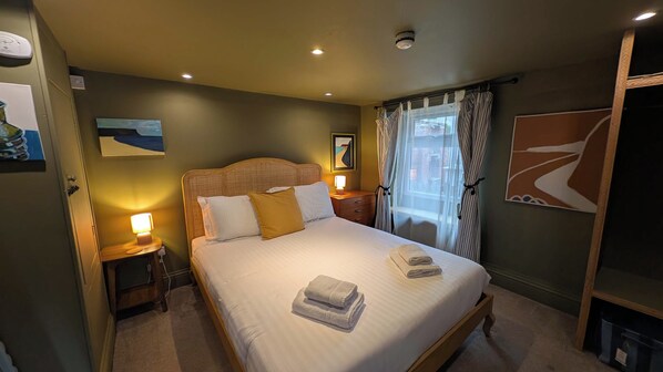 Habitación de hotel con cama, lámparas de noche, una ventana con cortinas y cuadros en las paredes.