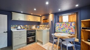 A compact kitchen with a stove, oven, and a dining area with a table and chairs. - Host & Stay | The Apartment, Mulgrave House (Hinderwell)