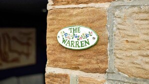 A stone wall with a sign that reads 'THE WARREN' and decorative floral elements. - Host & Stay | The Apartment, Mulgrave House (Hinderwell)