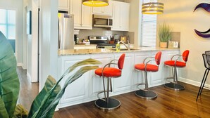 A modern kitchen with white cabinets, stainless steel appliances, and a central island with red bar stools. - Walkable to WW1 Museum - 10 Mins to DT - W&D on Site (Kansas City)
