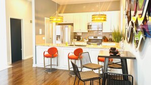 A modern kitchen with white cabinets, a stainless steel refrigerator, a double oven, and a dining area with bar stools. - Walkable to WW1 Museum - 10 Mins to DT - W&D on Site (Kansas City)