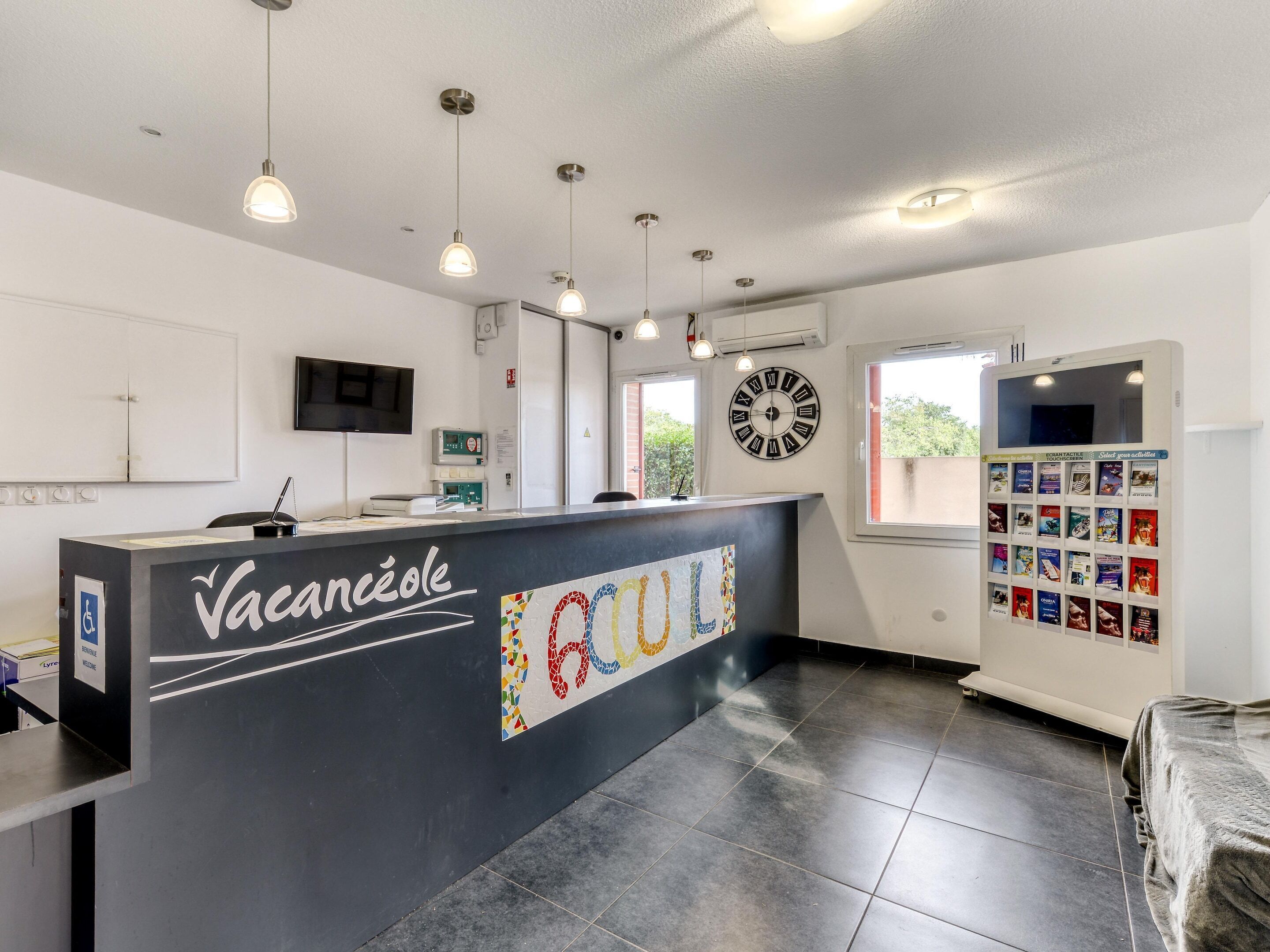 A reception area with a counter, a clock, a television, and a window with a view of greenery.