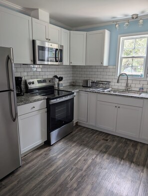 A kitchen with white cabinets, a stainless steel refrigerator, a microwave, a stove, and a sink. - Coastal Comfort Pet Friendly Beach Getaway Close to the Beach! Sleeps 6 (Supply)