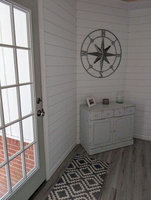 A room with a white door, a wall-mounted compass decoration, a white cabinet with drawers, and a patterned rug. - Coastal Comfort Pet Friendly Beach Getaway Close to the Beach! Sleeps 6 (Supply)