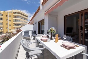 Ein Balkon mit Sitzgelegenheit, einem Esstisch gedeckt mit rosa Tellern und Gläsern, und einer Vase mit Blumen.