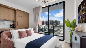 Ein modernes Hotelzimmer mit einem großen Bett, einer Küchenzeile, einem Balkon mit Blick auf die Stadt und einem Essbereich.