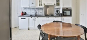 A kitchen with white cabinets, a stainless steel range hood, a coffee maker, and a dishwasher. - Le Nid Sablais  Maison 6 pers, jardin  garage au cœur des Sables (Les Sables-d´Olonne)