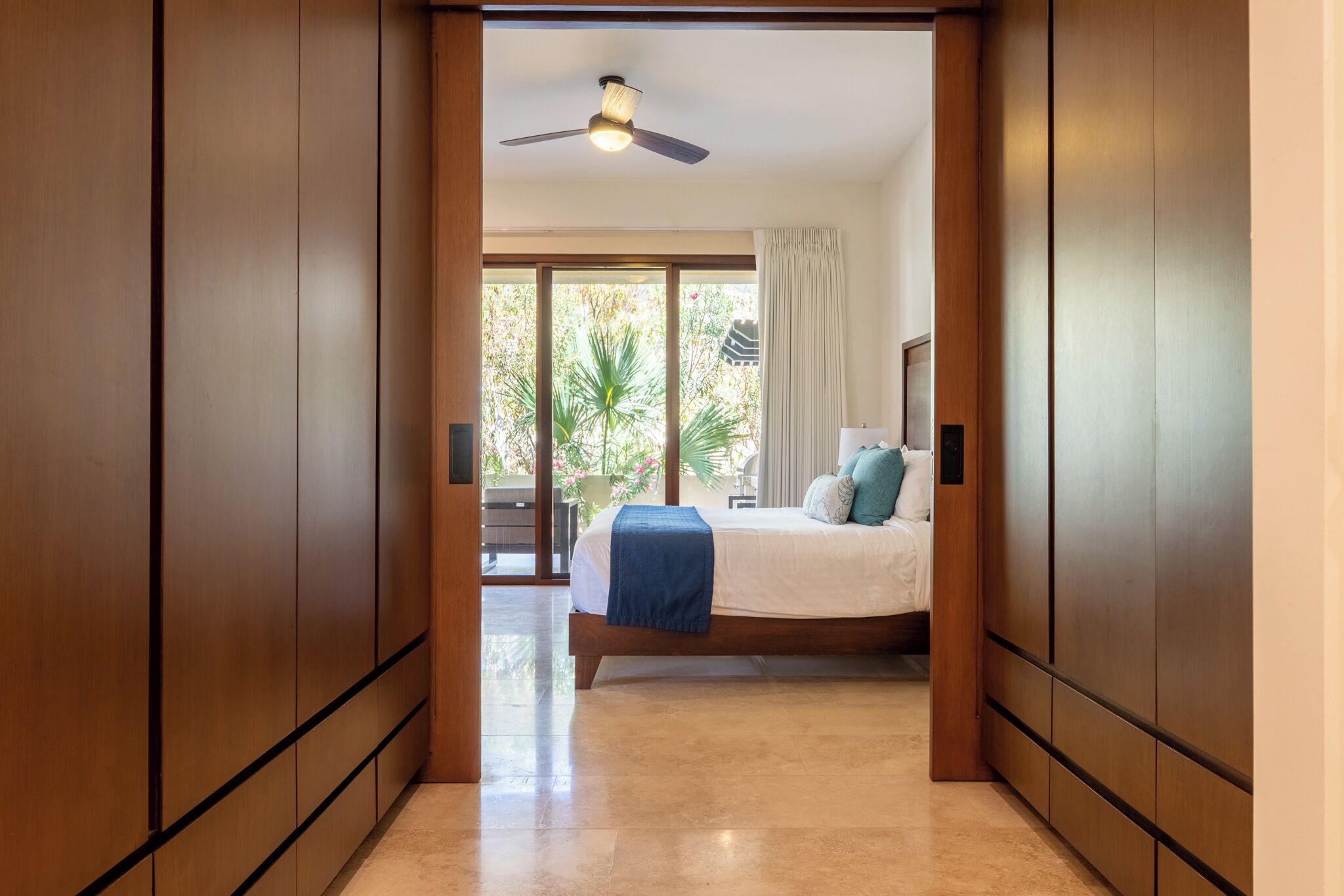 A bedroom with a bed, a ceiling fan, and a view of the outdoors.