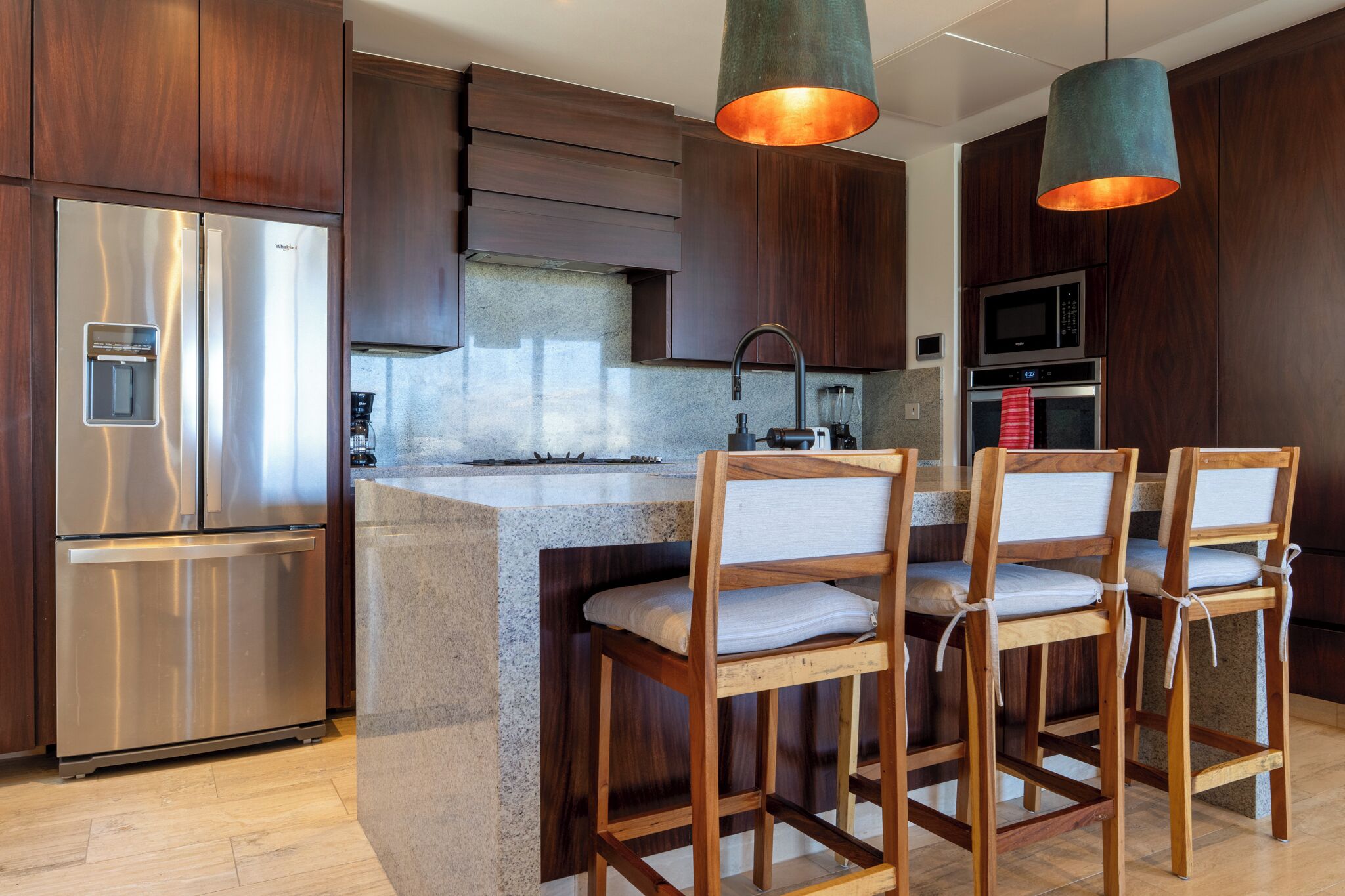 A modern kitchen with a central island, stainless steel appliances, and wooden bar stools.