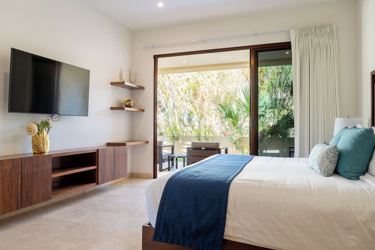 Un dormitorio con cama, televisor, consola de madera y un balcón con mesa y sillas.