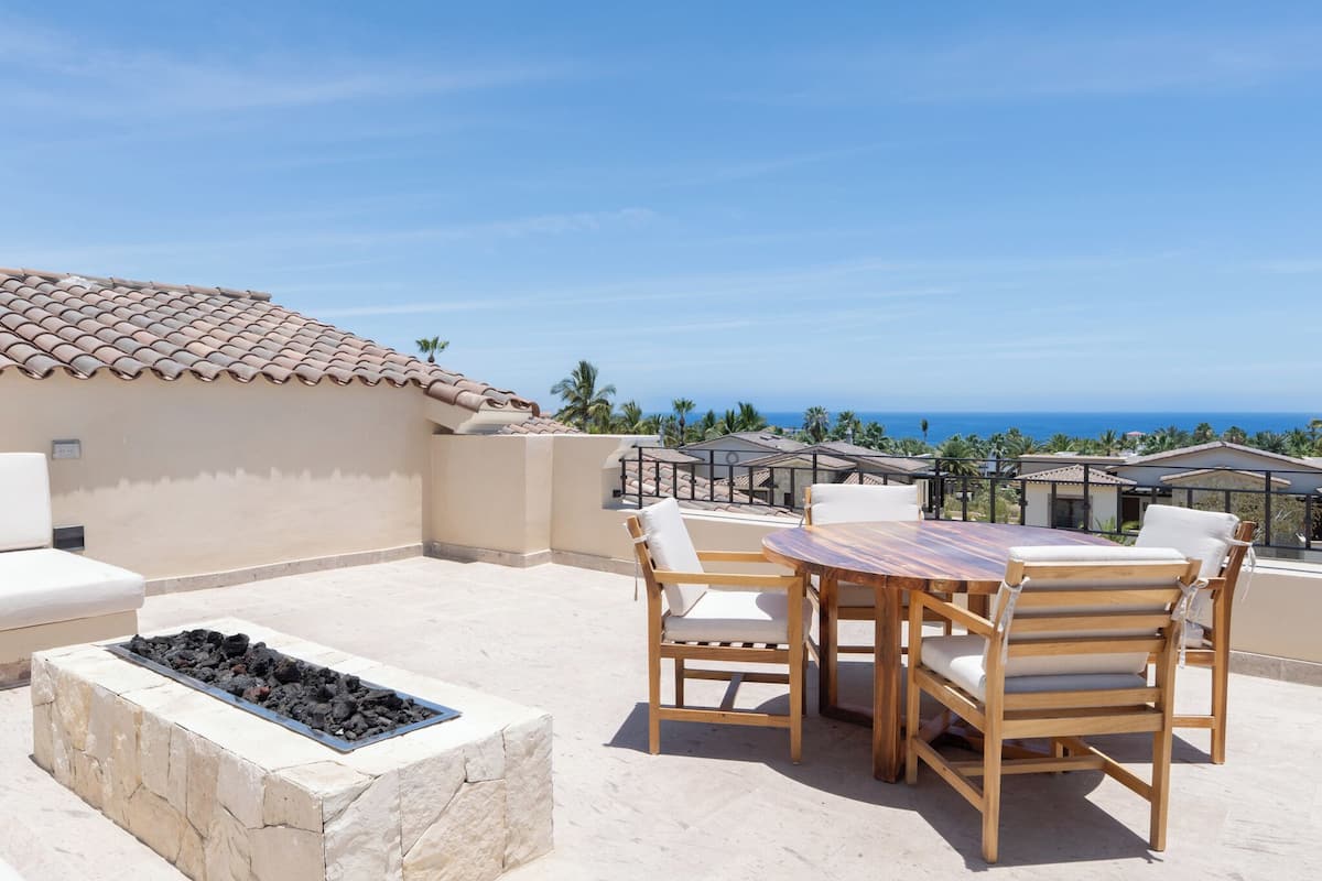 Un patio con mesa y sillas, una fogata y vistas al océano.