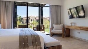 Un dormitorio con una cama grande, una silla, un televisor y vistas a una casa a través de una puerta corrediza.