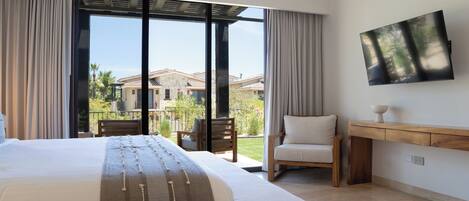 A bedroom with a large bed, a chair, a TV, and a view of a house through a sliding door.