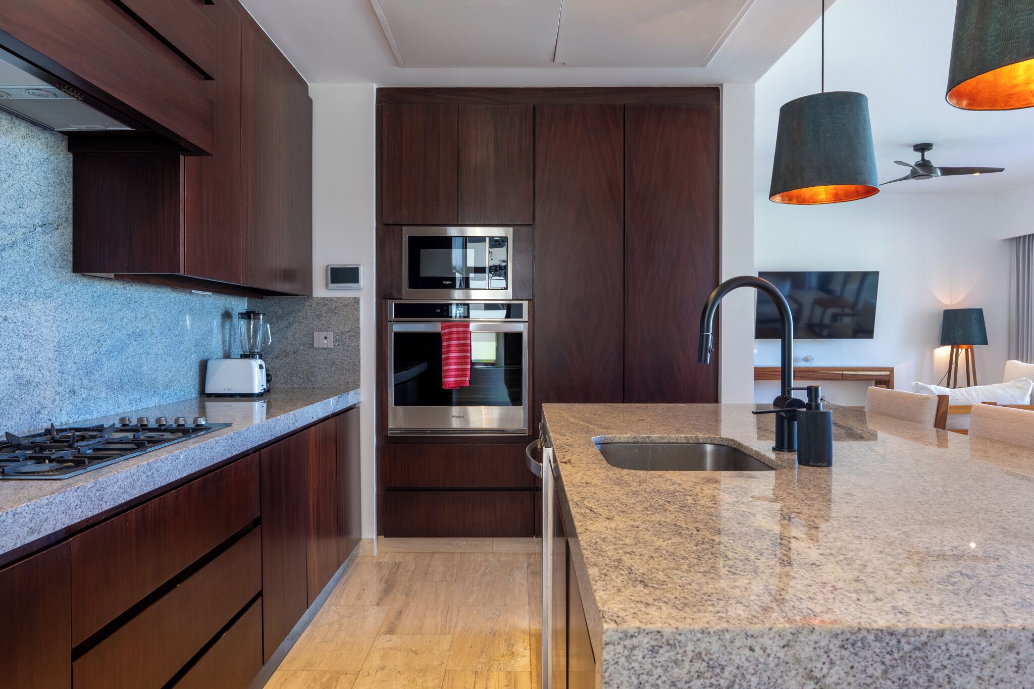 Una cocina moderna con armarios de madera oscura, electrodomésticos de acero inoxidable, encimeras de granito y horno empotrado.