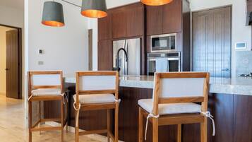 Een moderne keuken met donkerhouten kastjes, roestvrijstalen apparatuur en drie houten barkrukken met beklede zitplaatsen.