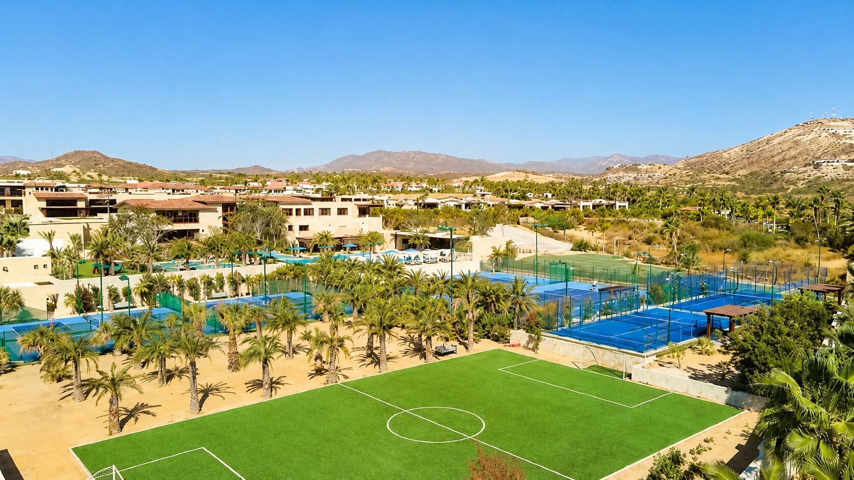 Un complejo turístico con varias canchas de tenis, una zona de piscina y un edificio grande con múltiples balcones.