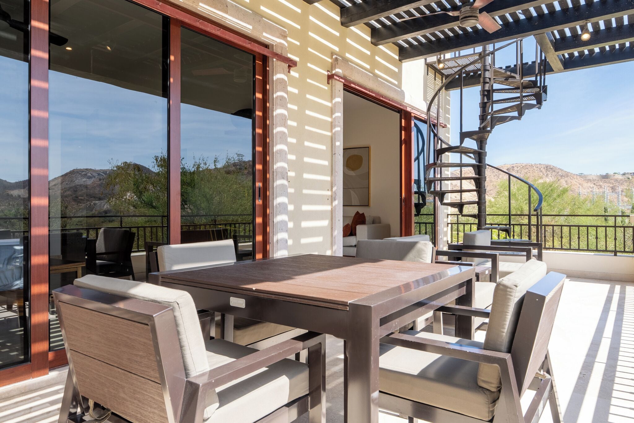 An outdoor patio with a dining table and chairs, a spiral staircase, and a view of the surrounding landscape.