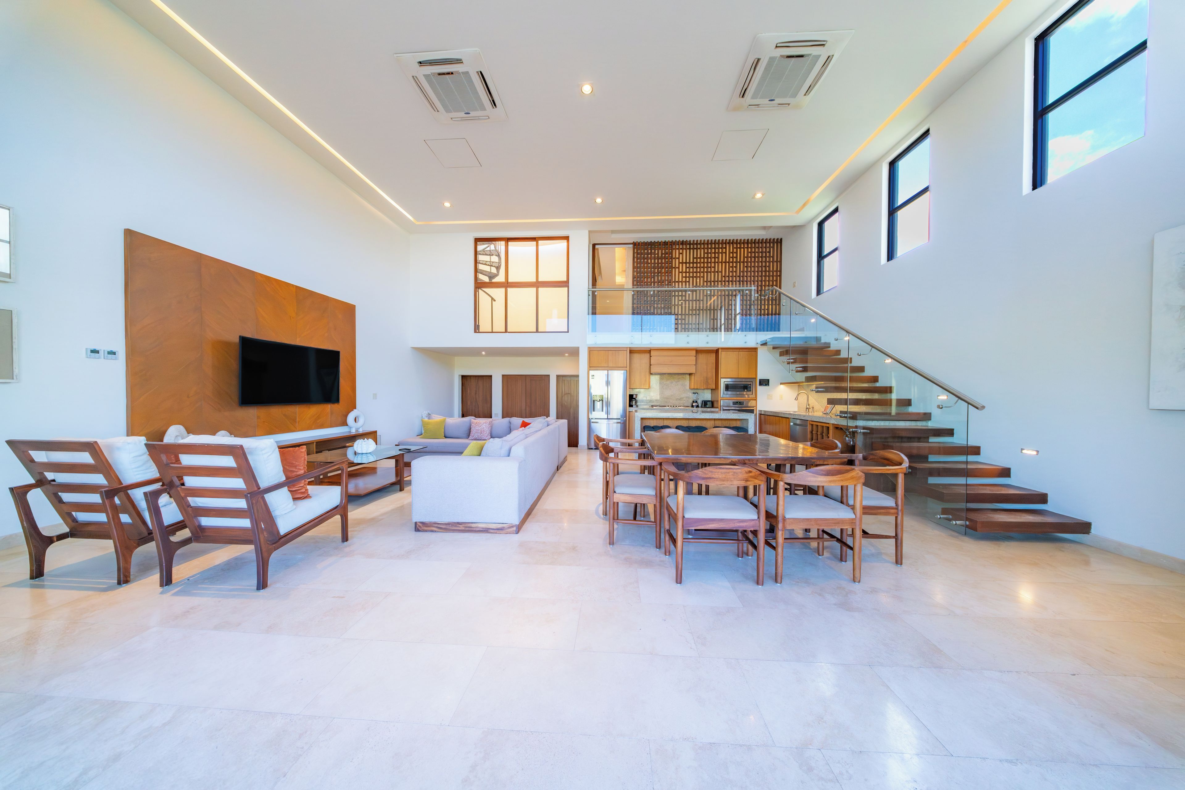 A spacious living area with a sofa, chairs, a TV, a staircase, and a kitchen.