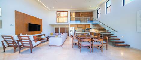 A spacious living area with a sofa, chairs, a TV, a staircase, and a kitchen.