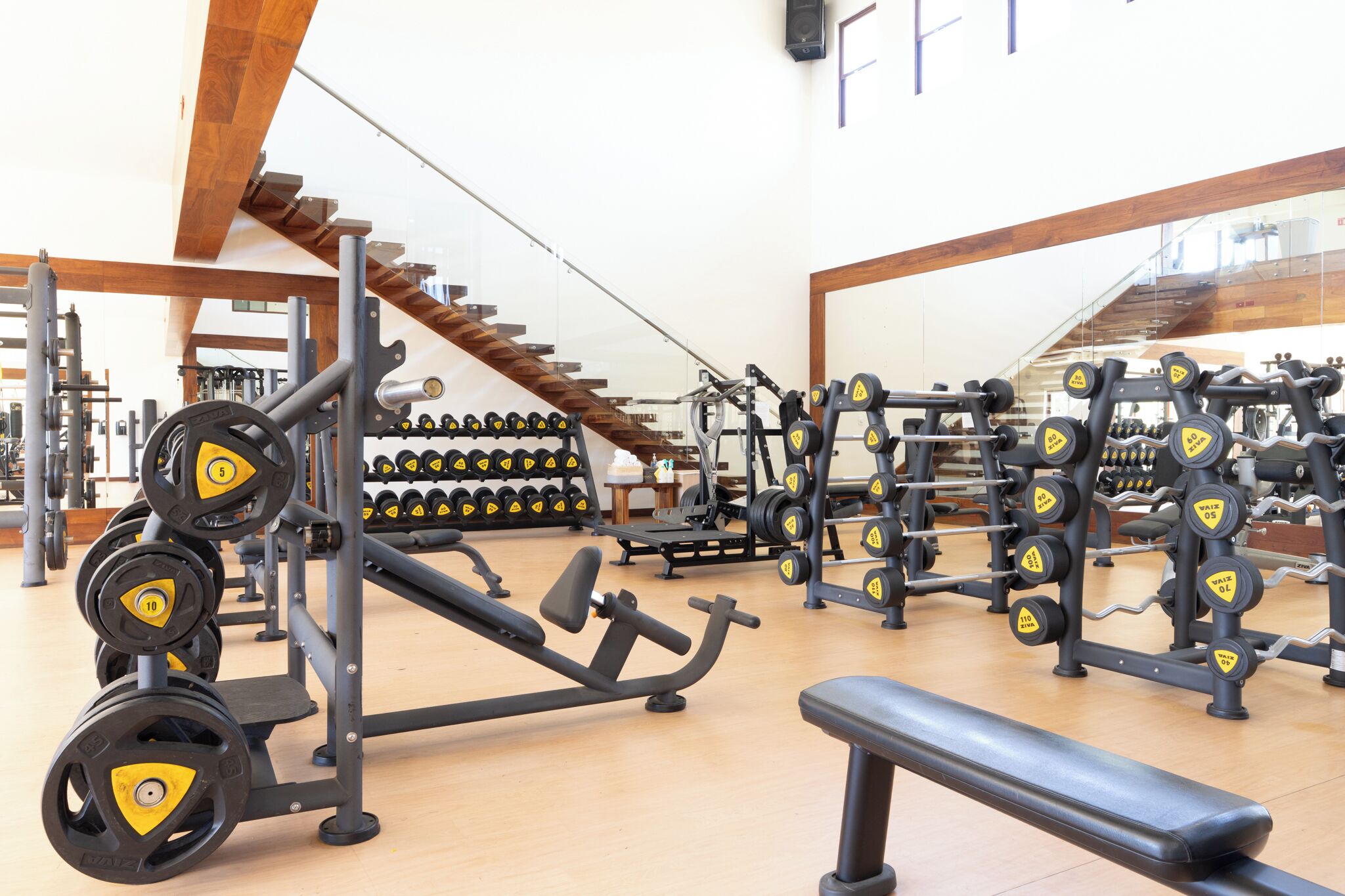 Uma academia com equipamentos de musculação, bancos e uma escada.