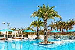 Un espace piscine aménagé avec des chaises longues, des parasols et des palmiers.