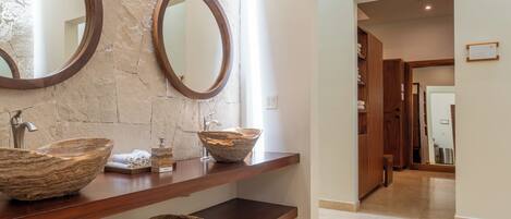 A bathroom with a stone wall, wooden vanity, two round mirrors, and a large bowl sink.