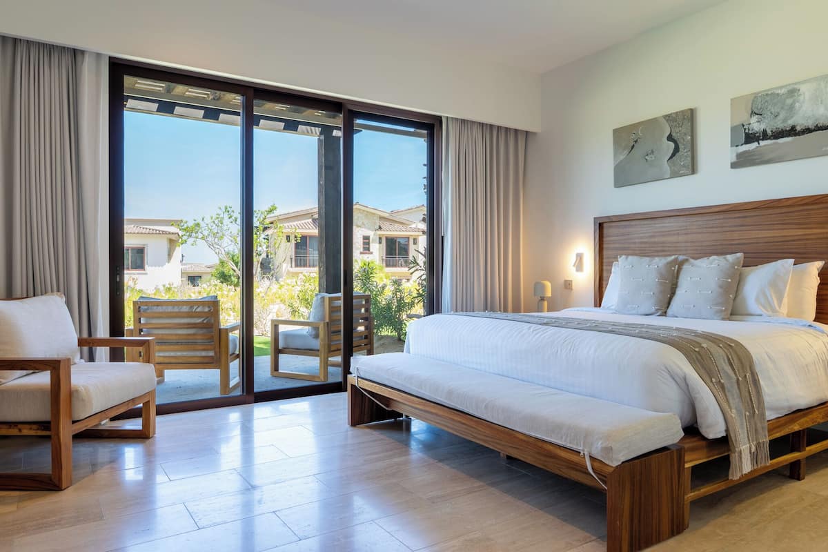 Un dormitorio con una cama grande, una silla, una mesa y vistas de edificios a través de un ventanal.