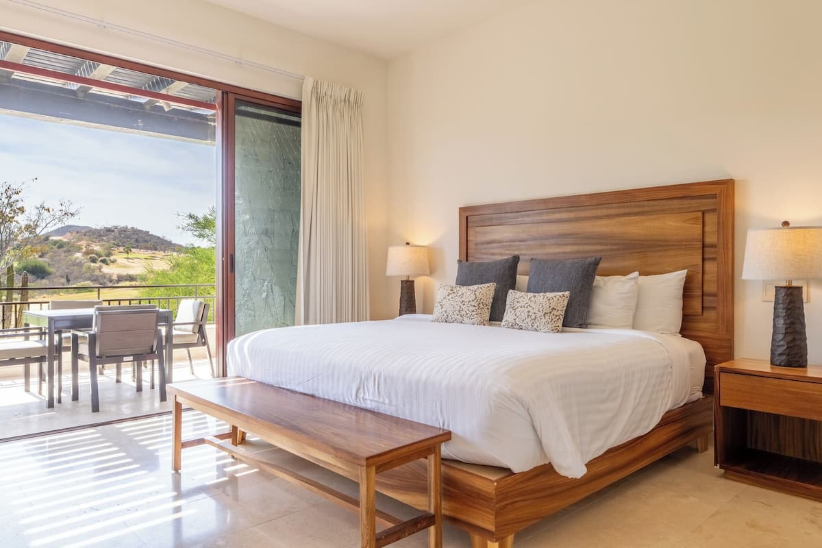 Un dormitorio con una cama grande, dos mesitas de noche, un banco y vistas a un paisaje verde.