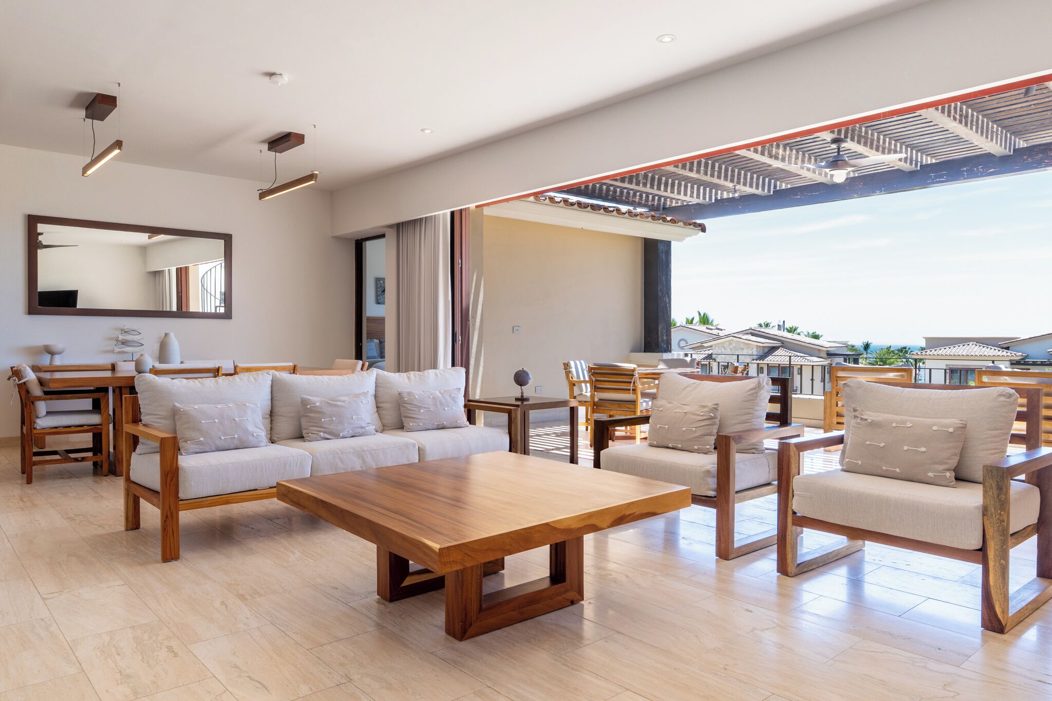 Amplia sala de estar con una mesa de centro de madera, sofás y sillones, un espejo grande y vistas al exterior.