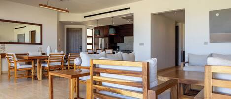 Un salon moderne avec des meubles en bois, un coin repas et une cuisine visible à travers une porte ouverte.