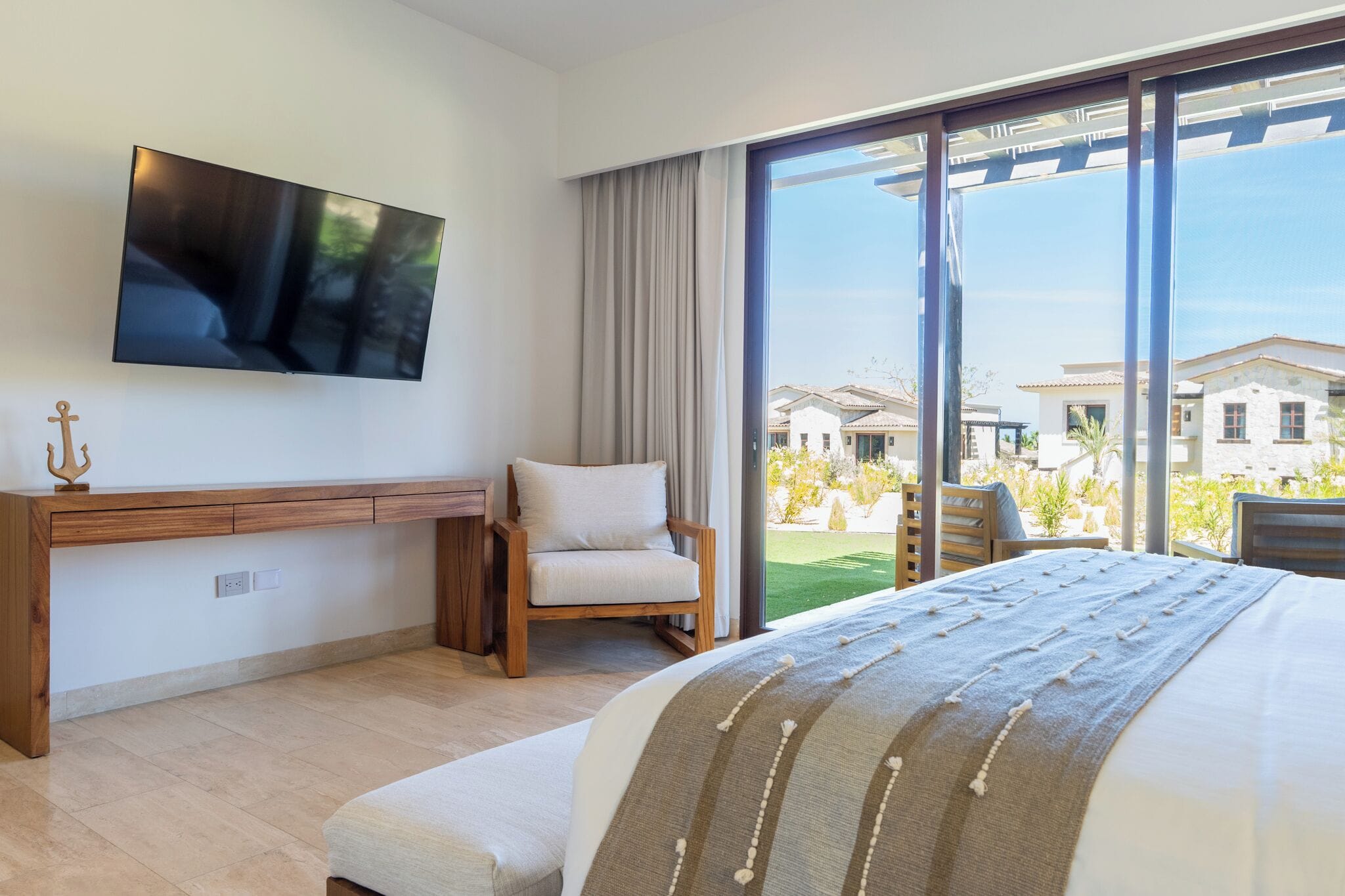 Quarto de hotel moderno com uma cama grande, uma TV na parede, uma escrivaninha de madeira e vista para a região através de amplas janelas.