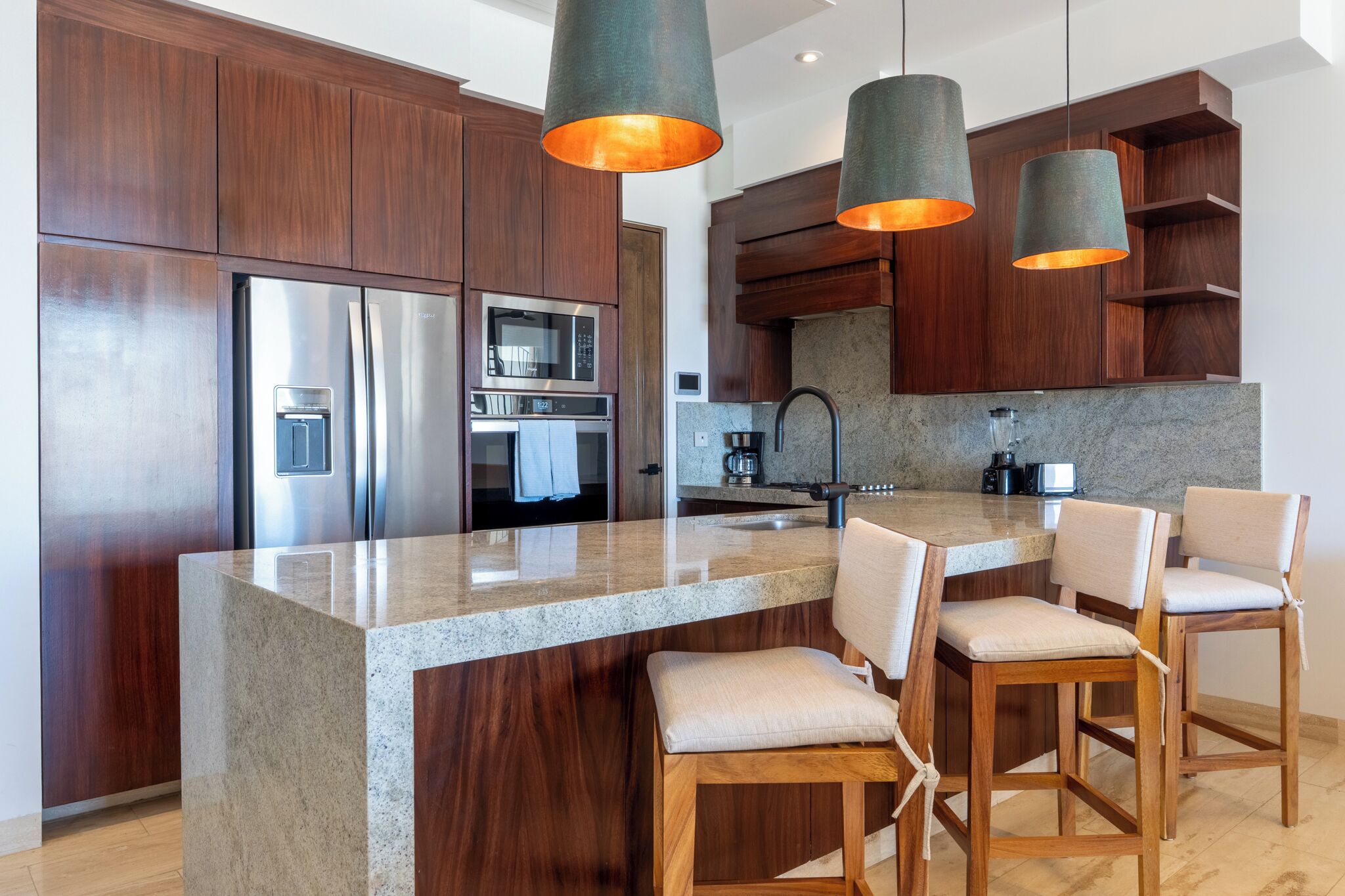 A modern kitchen with wooden cabinets, stainless steel appliances, a granite countertop, and pendant lighting.