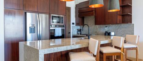 A modern kitchen with wooden cabinets, stainless steel appliances, a granite countertop, and pendant lighting.