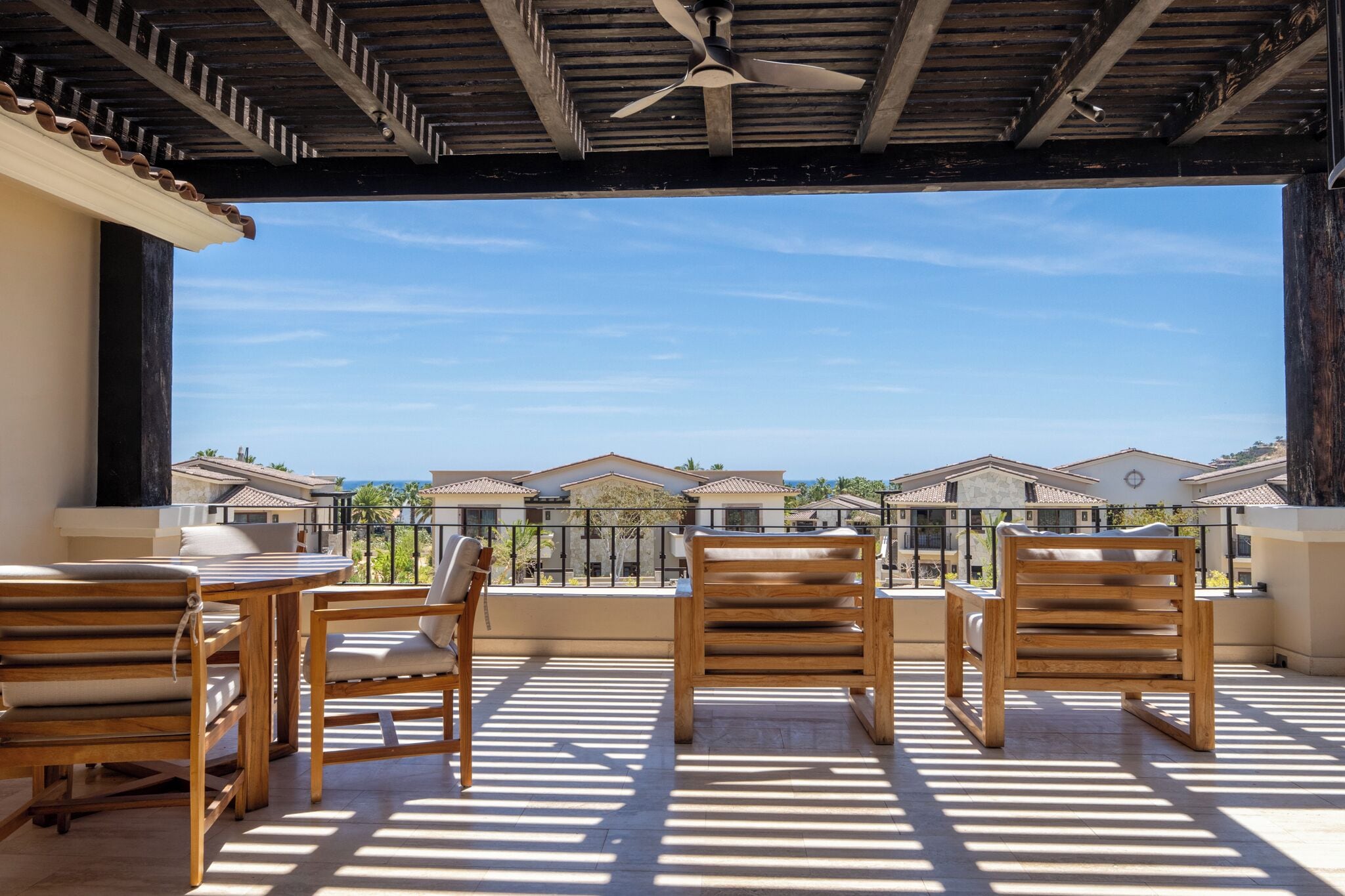 A balcony with wooden furniture and a ceiling fan, overlooking a residential area.