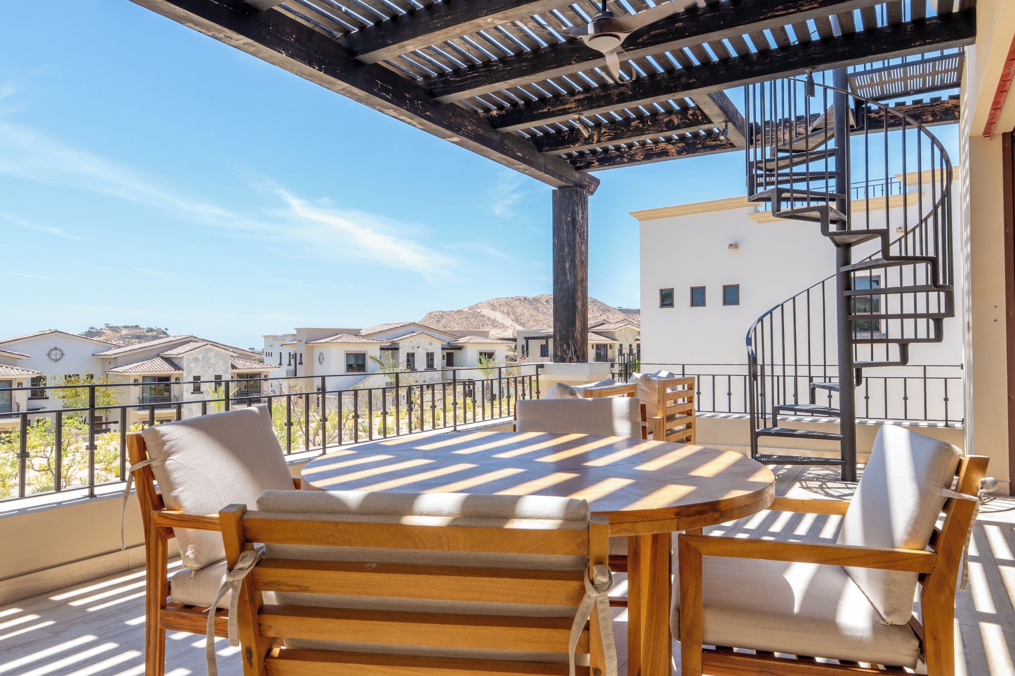 A balcony with wooden furniture, a pergola, and a spiral staircase.