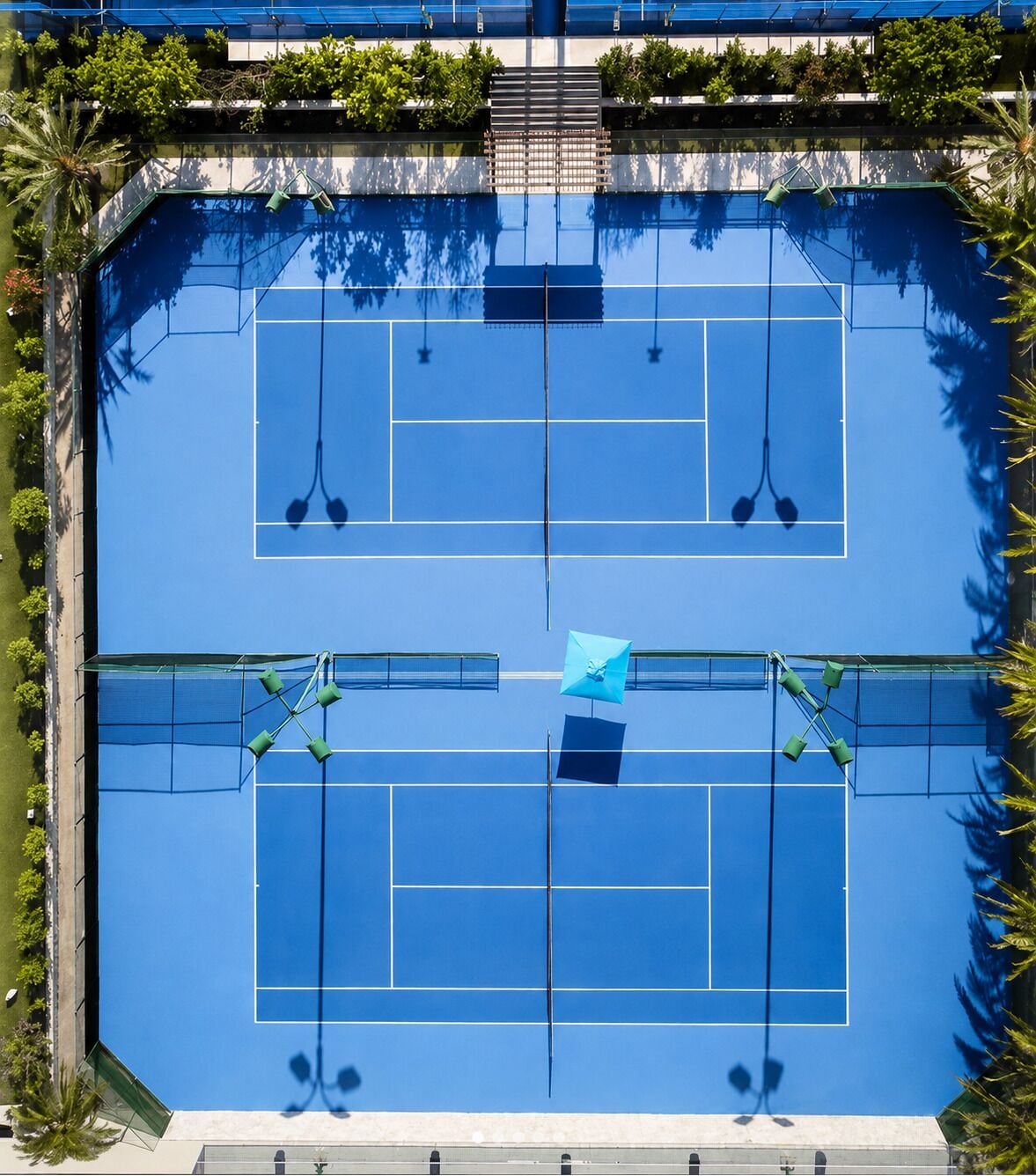 Vista aérea de uma quadra de tênis com vegetação ao redor e uma piscina.