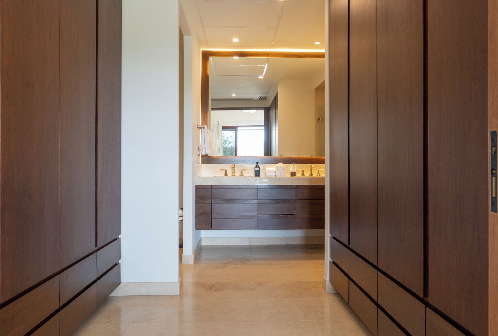 A hallway with wooden cabinets and a vanity with a mirror.